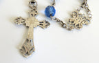 Silver cross pendant on a chain with blue beads against a white background