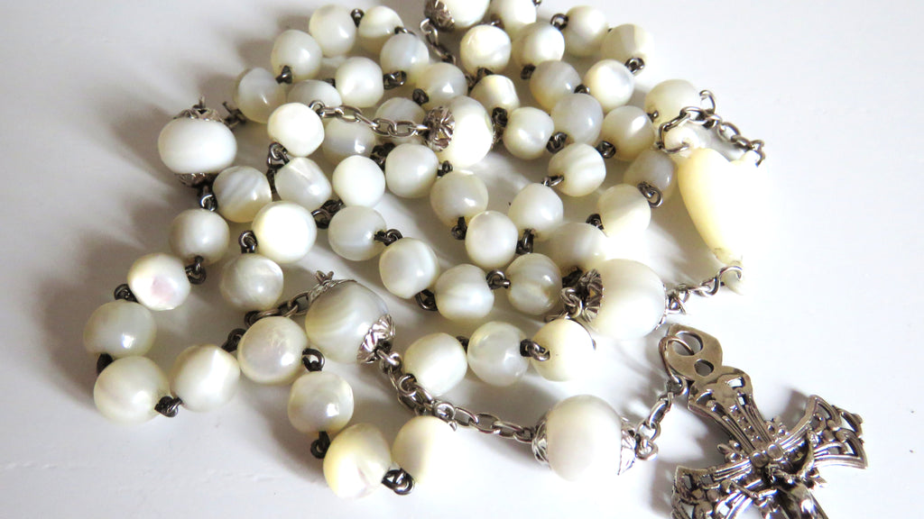 White beaded rosary with a silver cross on a white background