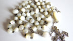 White beaded rosary with a silver cross on a white background