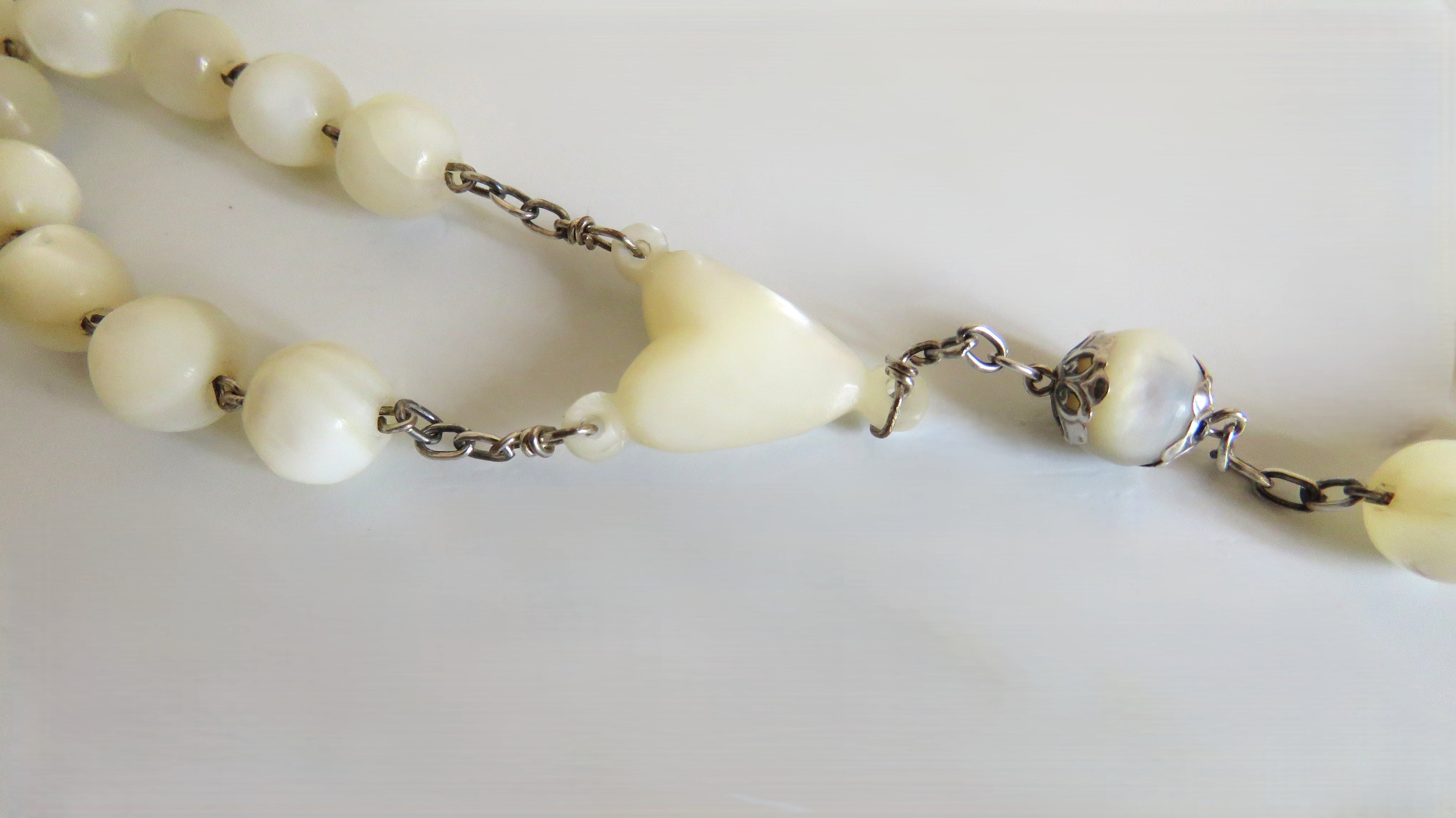 Necklace with white beads and a heart-shaped centre on a light background