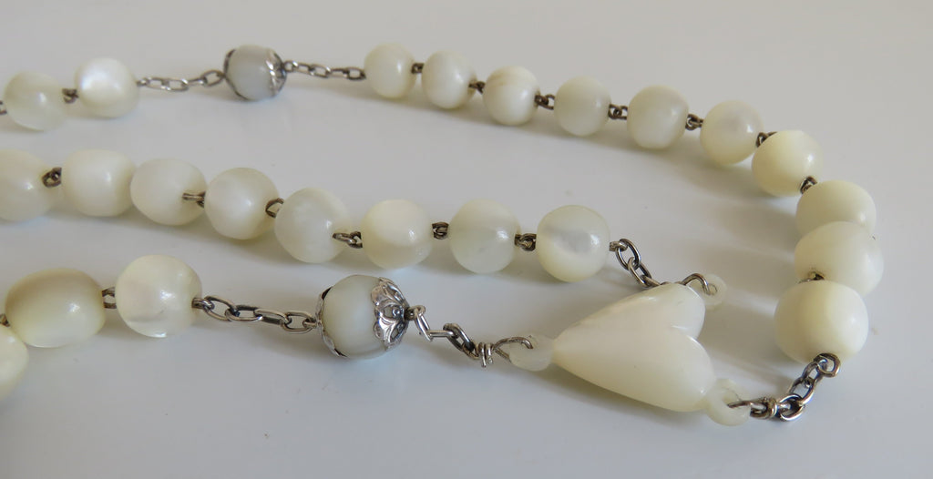 White rosary with a mouther of pearl heart on a white background
