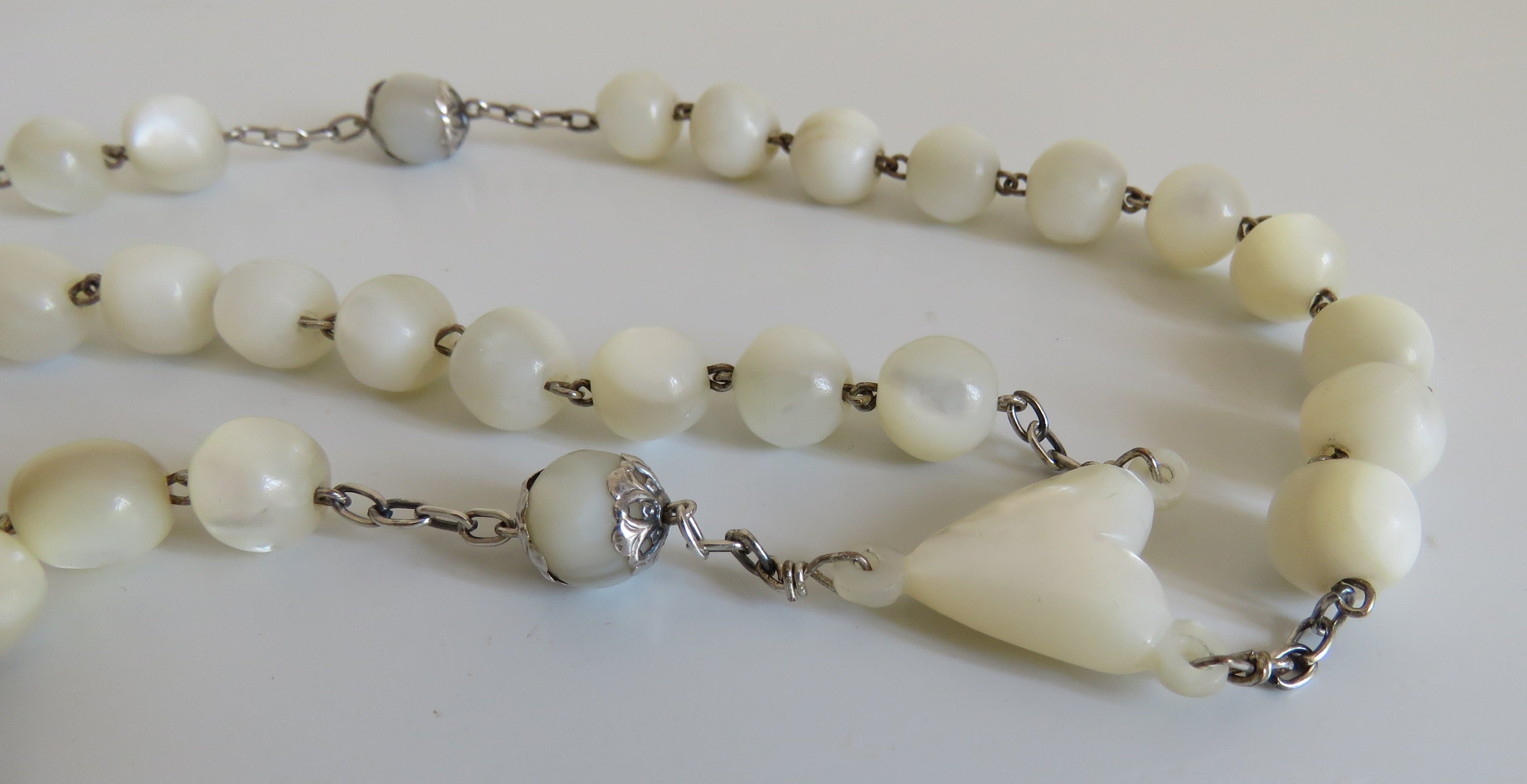 White rosary with a mouther of pearl heart on a white background
