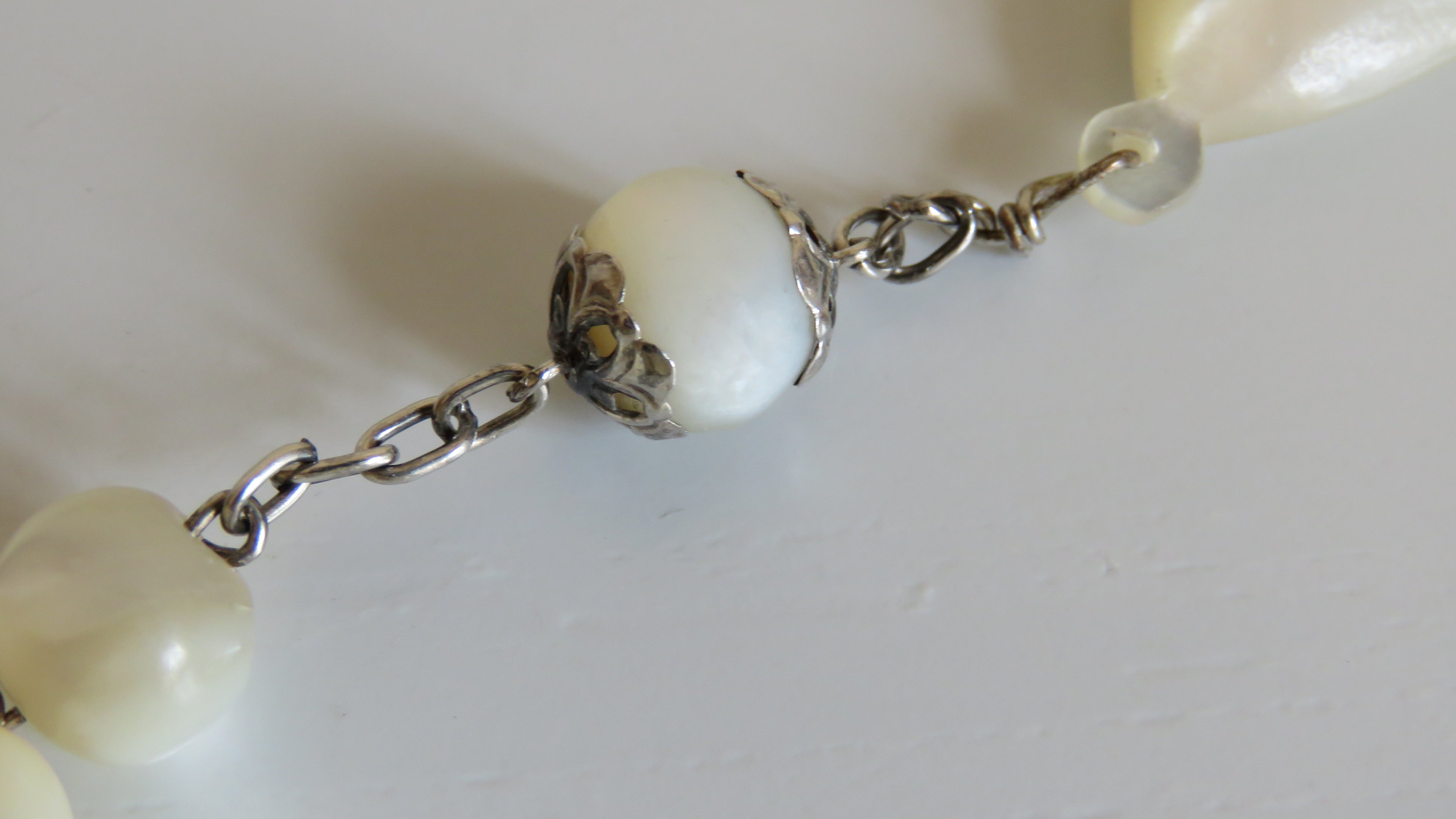 Close-up of a necklace with white beads and silver chain on a light background