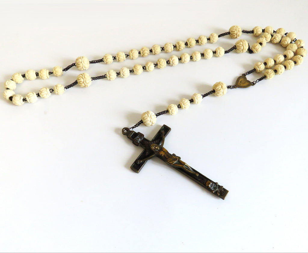 A traditional Catholic rosary featuring cream-colored bone beads and crucifix pendant, laid out on a plain white background.