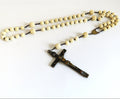 A traditional Catholic rosary featuring cream-colored bone beads and crucifix pendant, laid out on a plain white background.