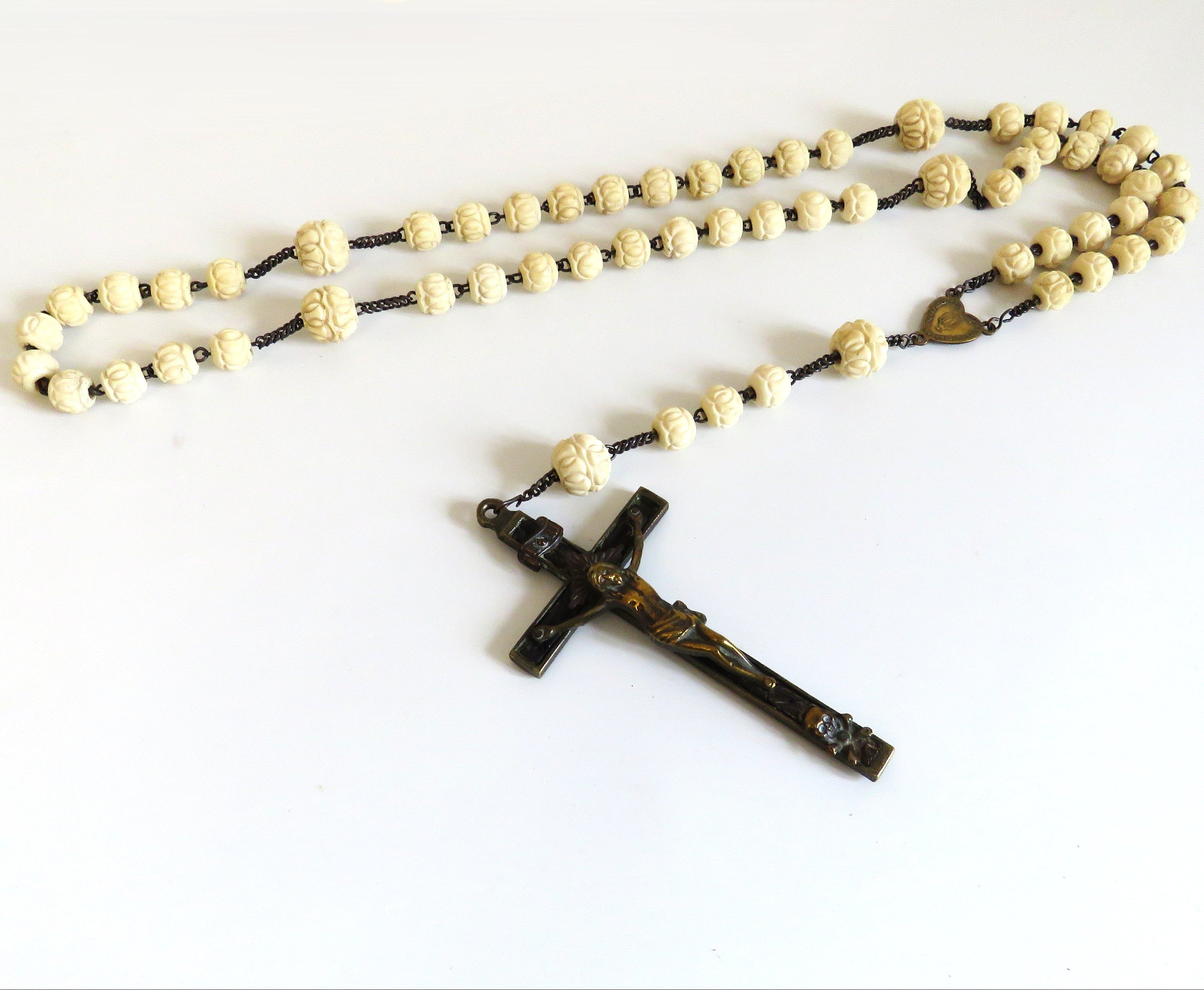 A traditional Catholic rosary featuring cream-colored bone beads and crucifix pendant, laid out on a plain white background.