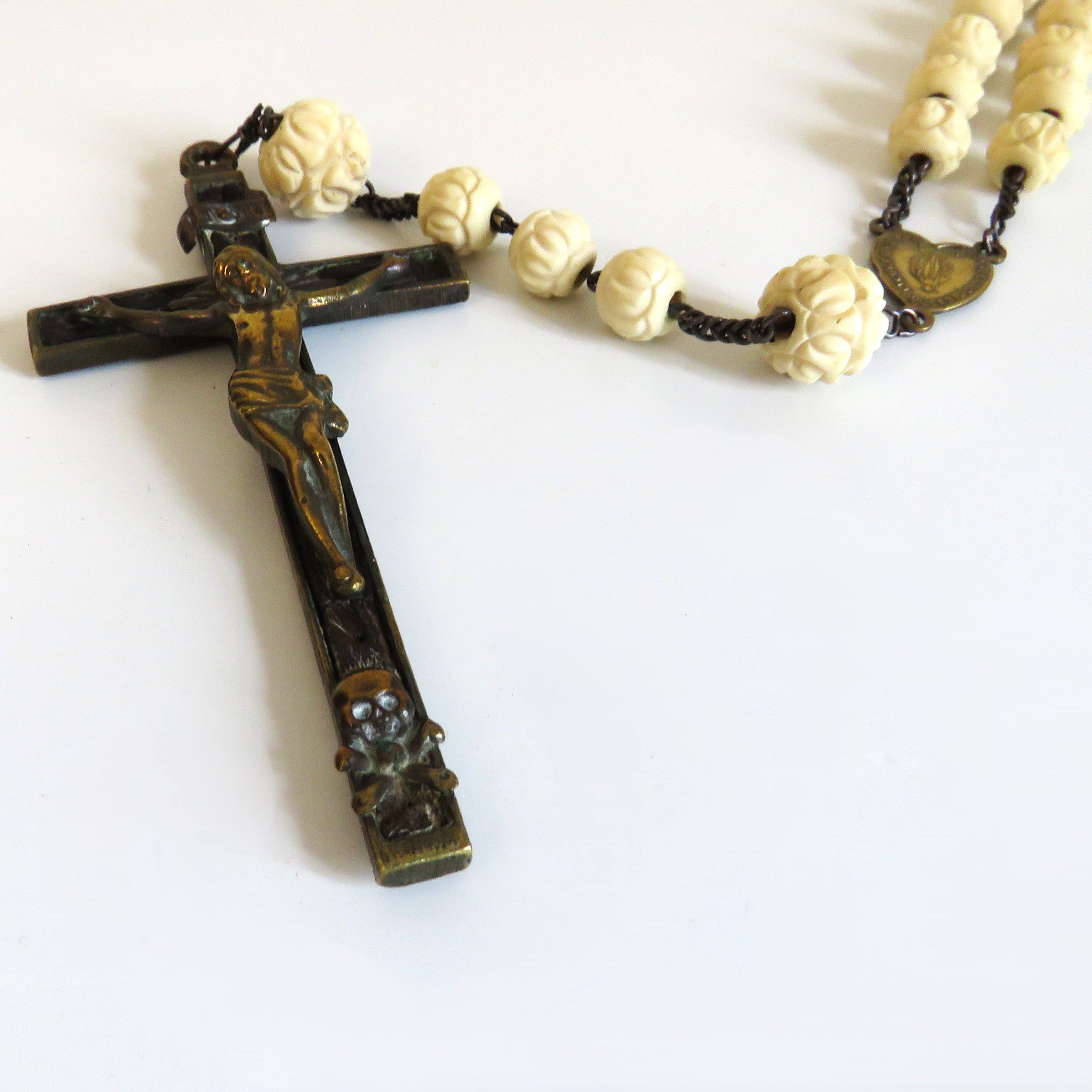 A vintage rosary with a dark bronze crucifix and cream-colored bone beads on a plain white background.