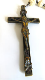 A dark metal crucifix pendant necklace featuring a raised figure of Jesus Christ on a cross with a skull at the bottom, shown against a plain white background.