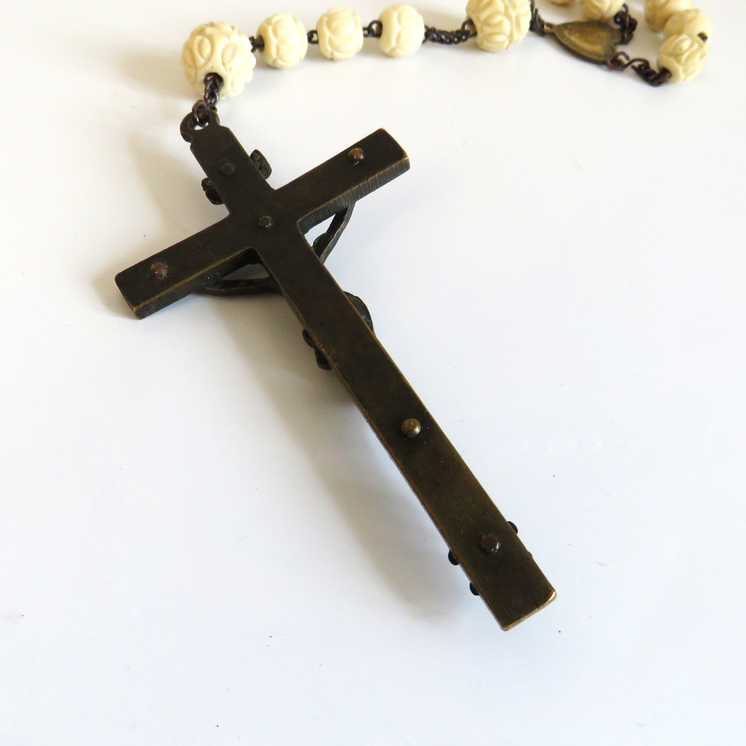 A dark metal crucifix pendant with a rosary featuring cream-colored beads, displayed on a plain white background.