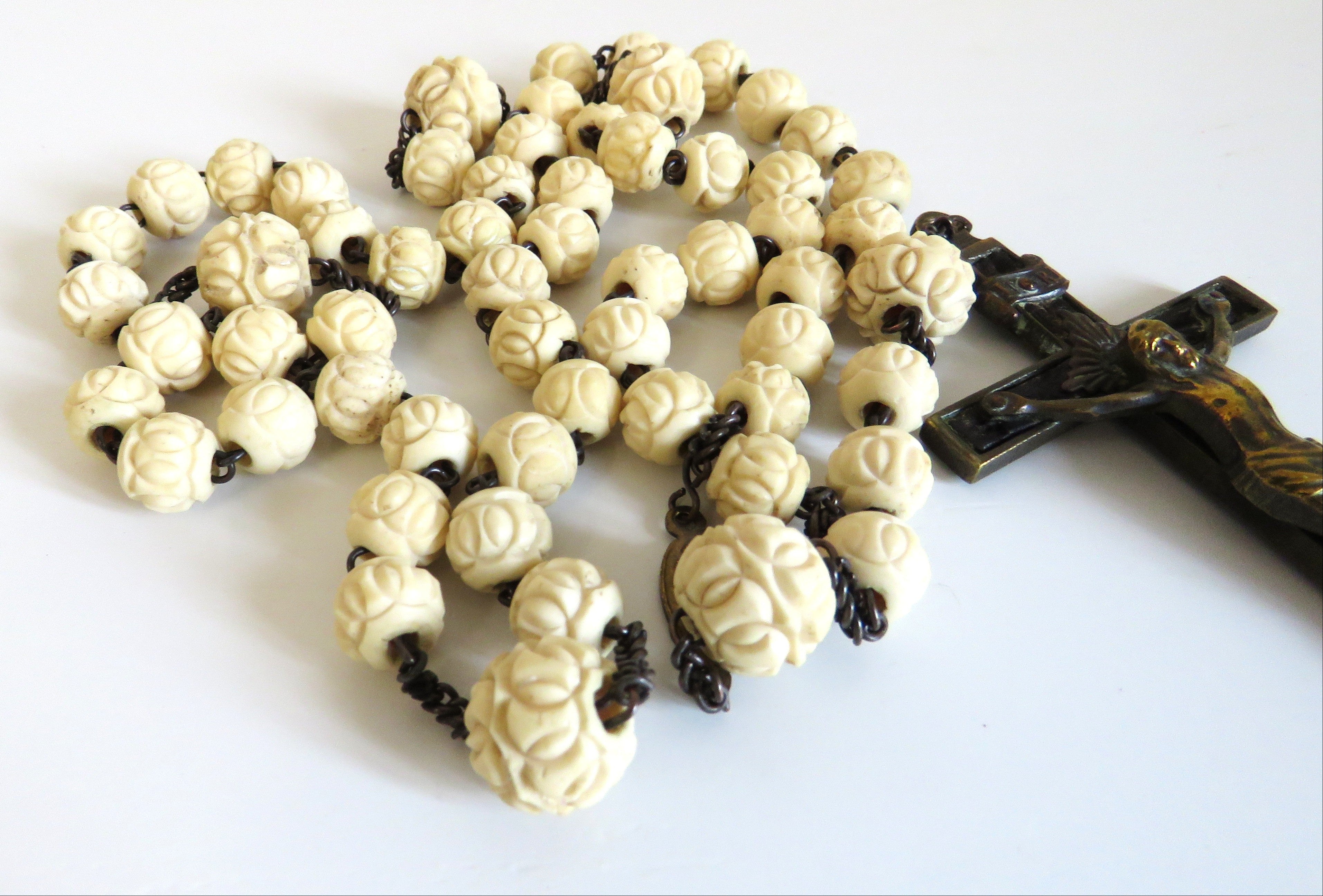 A rosary with cream-colored, intricately carved bone  beads and featuring a dark wooden crucifix on a plain white background.