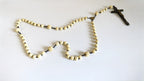 A rosary with cream-colored bone beads featuring a dark metal crucifix and centerpiece, laid out on a plain white surface.