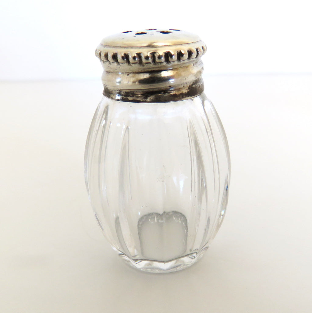 Clear glass salt shaker with silver lid on a white background