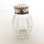 Clear glass salt shaker with silver lid on a white background