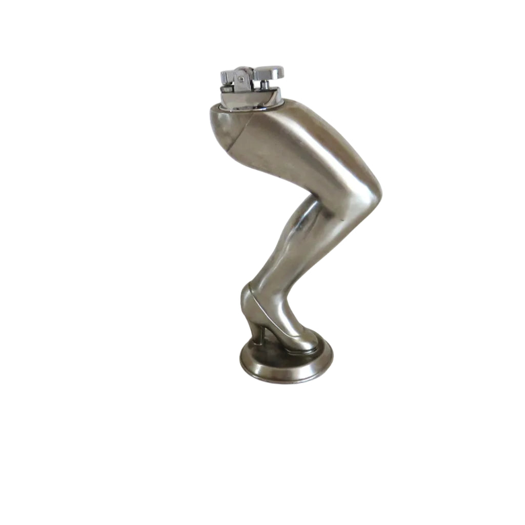A cigarette lighter on a metallic silver sculpture of a bent leg wearing a high heel, standing on a round base against a plain white background.