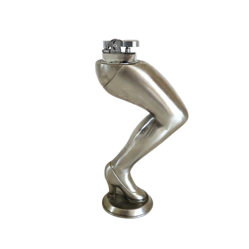 A cigarette lighter on a metallic silver sculpture of a bent leg wearing a high heel, standing on a round base against a plain white background.