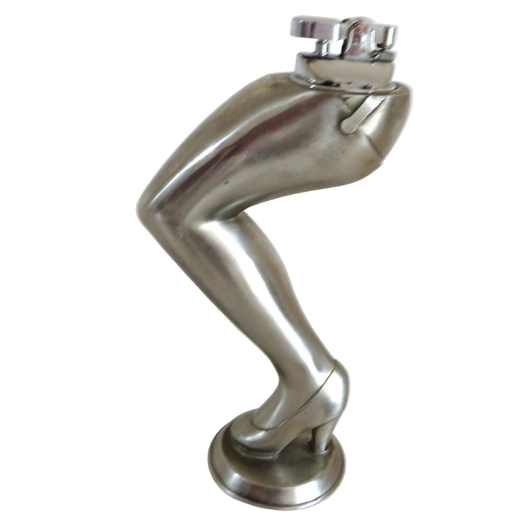 A cigarette lighter on a metallic silver sculpture of a bent leg wearing a high heel, standing on a round base against a plain white background.