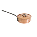 A copper saucepan with a matching lid and a long black handle, resting on a white wooden table against a white wall.