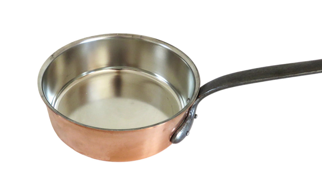 A copper saucepan tin lined with a black handle, shown on a white wooden surface.