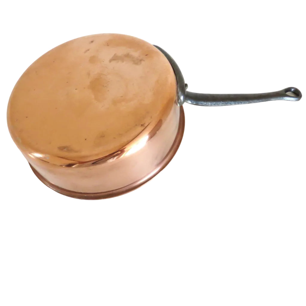 A copper saucepan with a black handle resting on a white wooden surface.