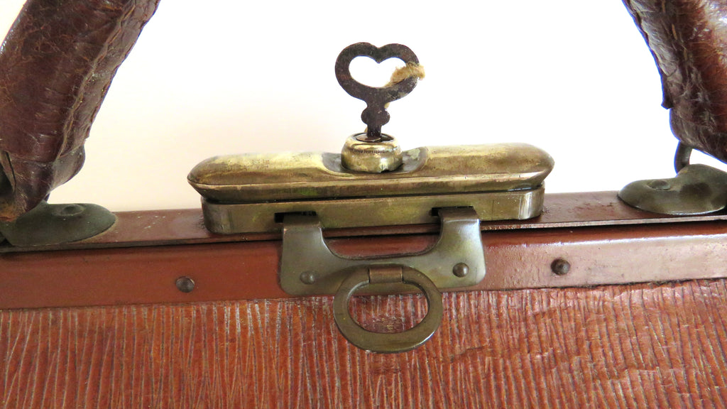 Close-up of an antique wooden trunk or suitcase with a brass latch and a small heart-shaped key on a white background.