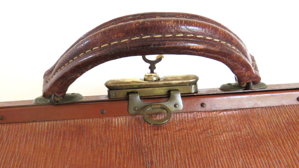 Close-up of a vintage brown leather suitcase handle with brass hardware and a textured wood-grain front panel.