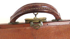 Close-up of a vintage brown leather suitcase handle with brass hardware and a textured wood-grain front panel.