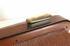 Close-up of a vintage brown leather clutch or case with a brass clasp on a light background.