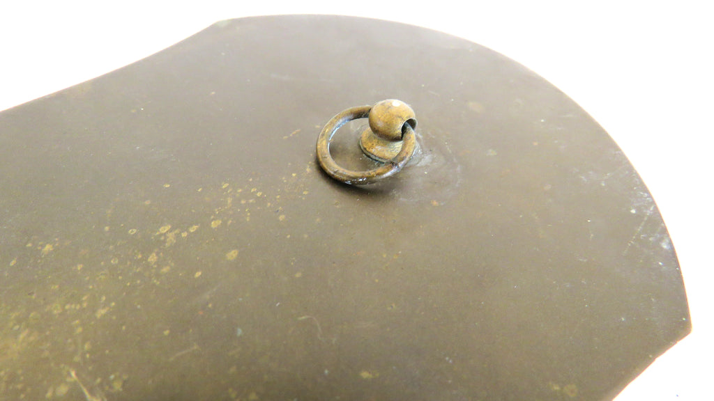 A close-up of a dark metallic surface with a small circular ring detail and a round knob, photographed against a white background.
