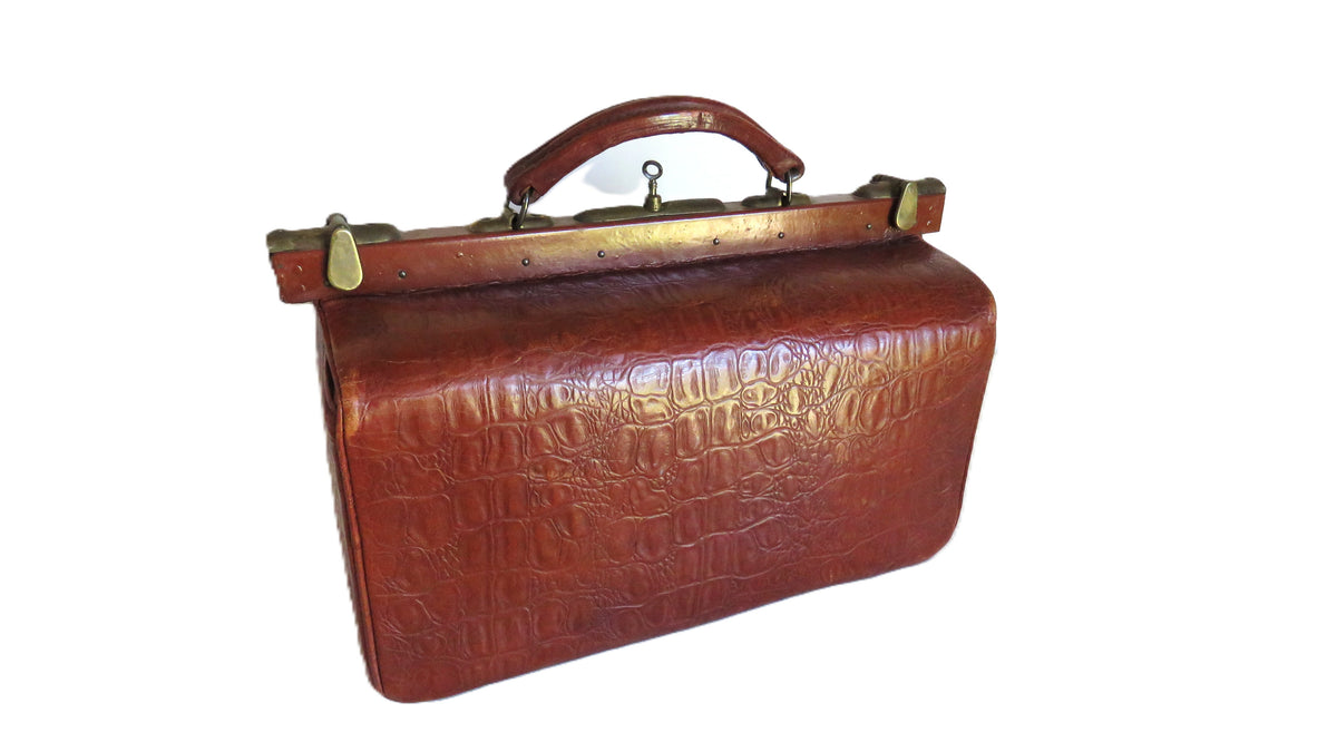 A vintage brown embossed leather briefcase-style handbag with a top handle and brass-tone metal frame closure, shown on a plain white background.