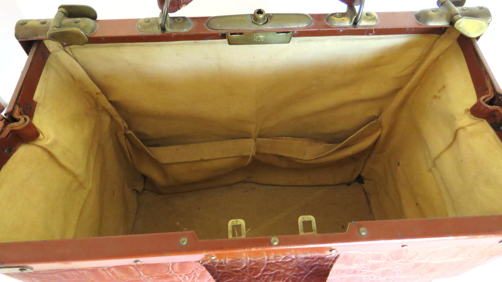 An open vintage-style trunk or suitcase with a brown leather exterior and a tan canvas interior lining, showing the empty compartment and metal latch hardware.
