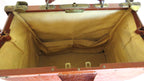 An open vintage-style trunk or suitcase with a brown leather exterior and a tan canvas interior lining, showing the empty compartment and metal latch hardware.
