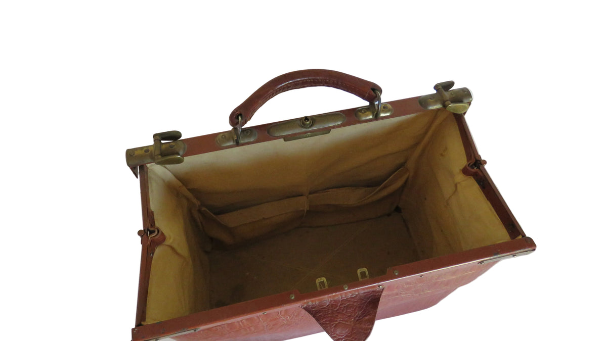 An open vintage-style brown leather suitcase or trunk with brass hardware and a tan fabric lining, photographed on a white table against a white wall.