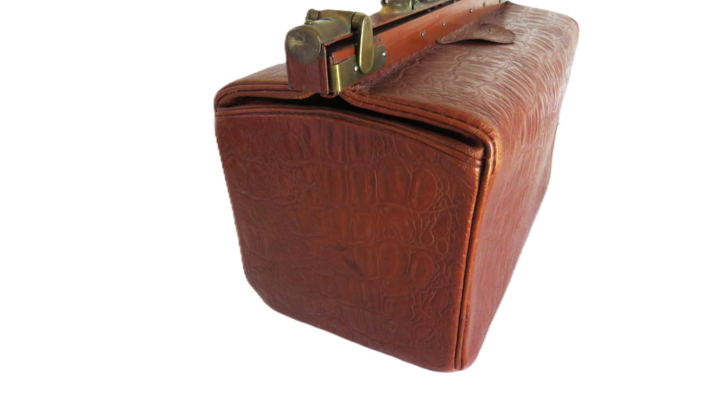 A vintage brown leather briefcase with an embossed crocodile pattern, brass hardware, and a top handle, shown on a plain white background.
