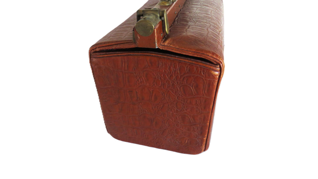 A close-up of a brown embossed leather case or briefcase corner with a brass-toned clasp, isolated on a white background.