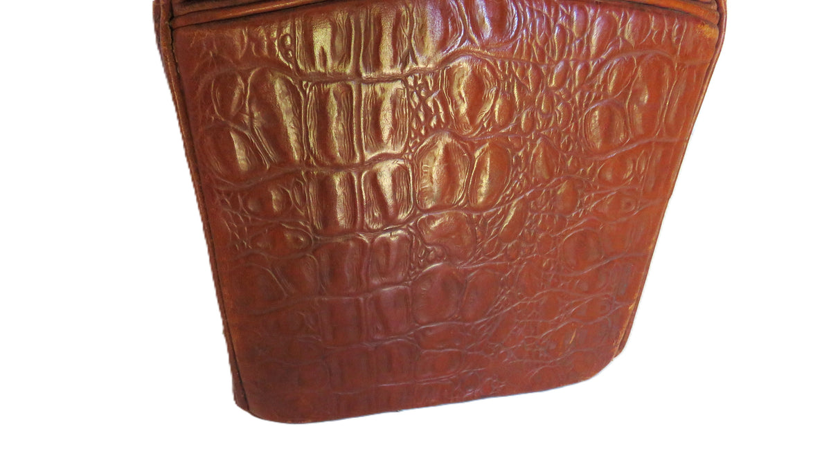 A close-up of a brown crocodile-embossed leather material, showing a glossy textured pattern on a plain white background.