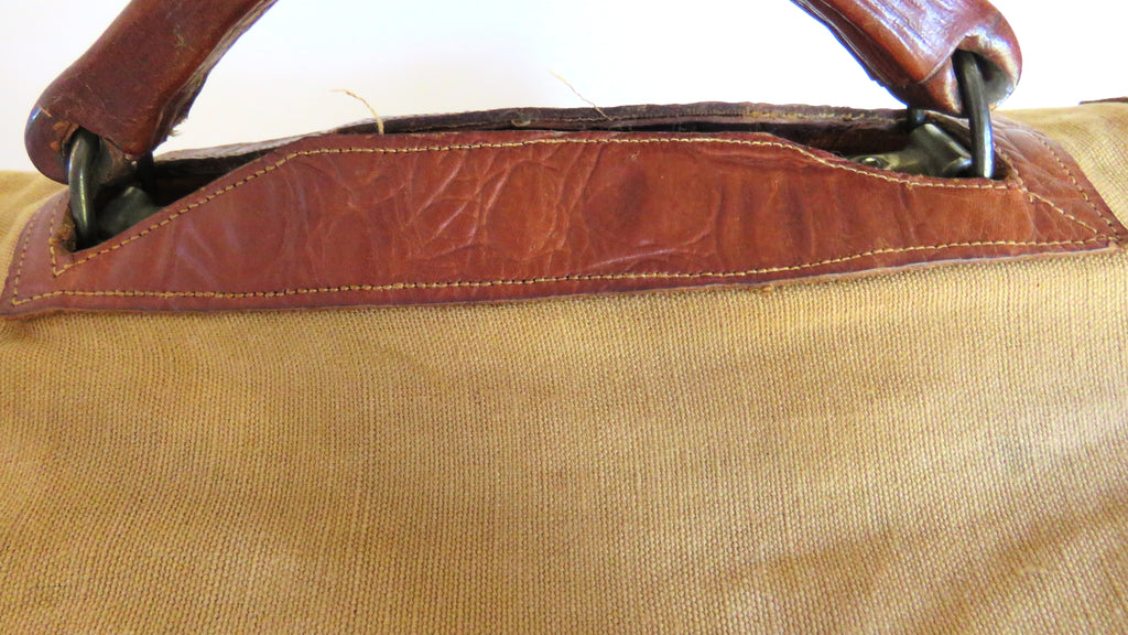 Close-up of a canvas bag with a tan body and reddish-brown leather trim and handles.