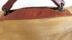 Close-up of a canvas bag with a tan body and reddish-brown leather trim and handles.