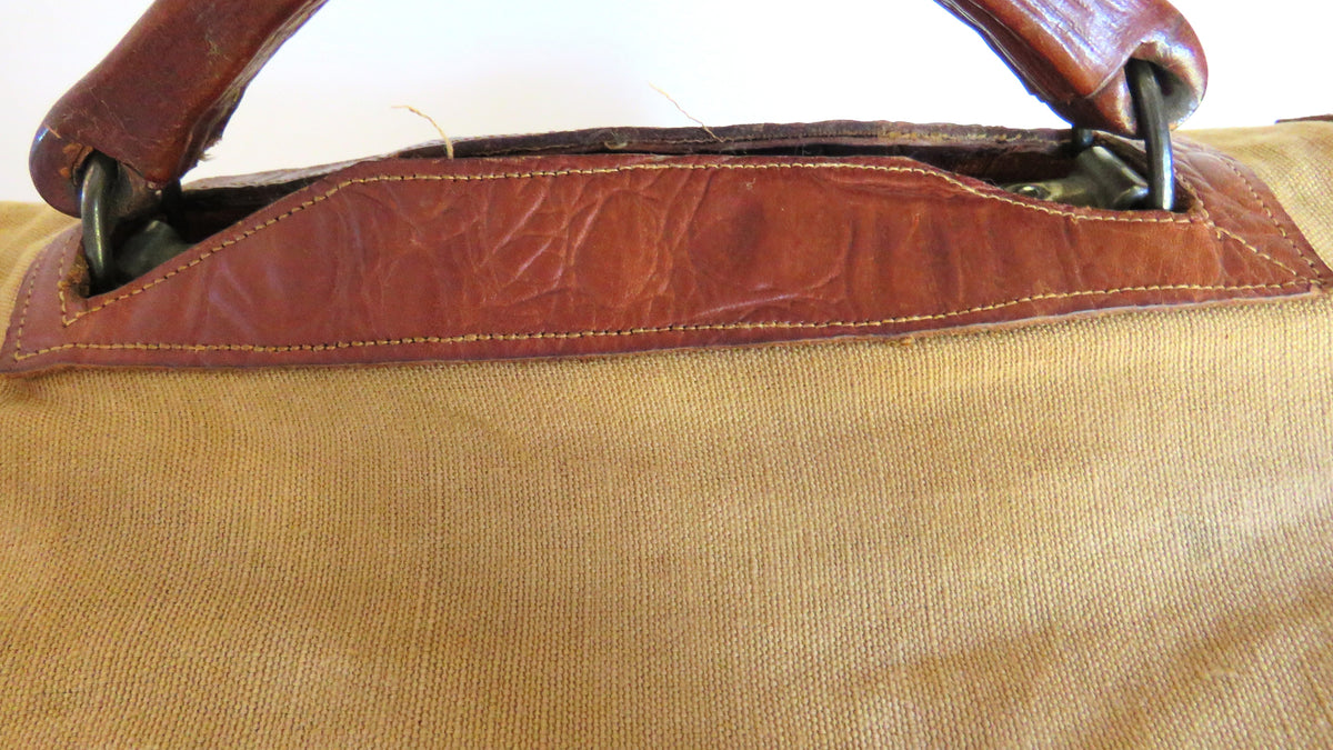 Close-up of a canvas bag with a tan body and reddish-brown leather trim and handles.
