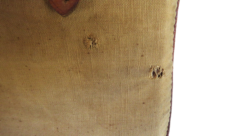 Close-up of a beige canvas or linen fabric item with visible texture, small circular stitched details, and a brown edge, shown against a white background.