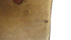 Close-up of a beige canvas or linen fabric item with visible texture, small circular stitched details, and a brown edge, shown against a white background.