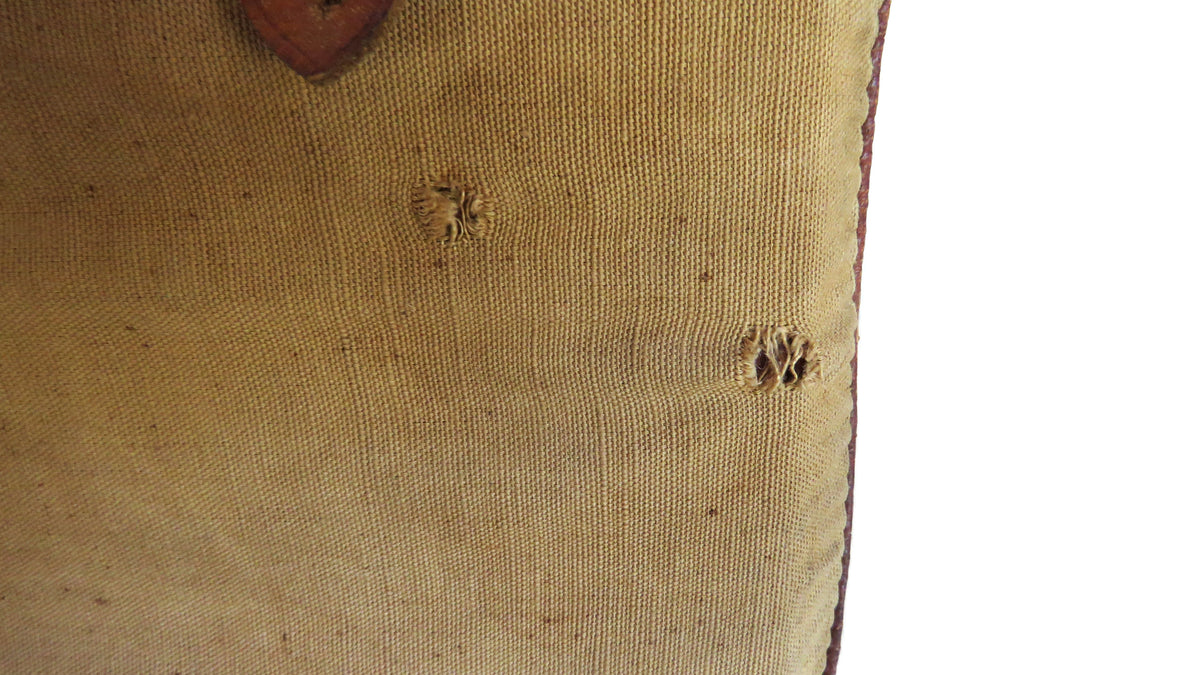Close-up of a beige canvas or linen fabric item with visible texture, small circular stitched details, and a brown edge, shown against a white background.