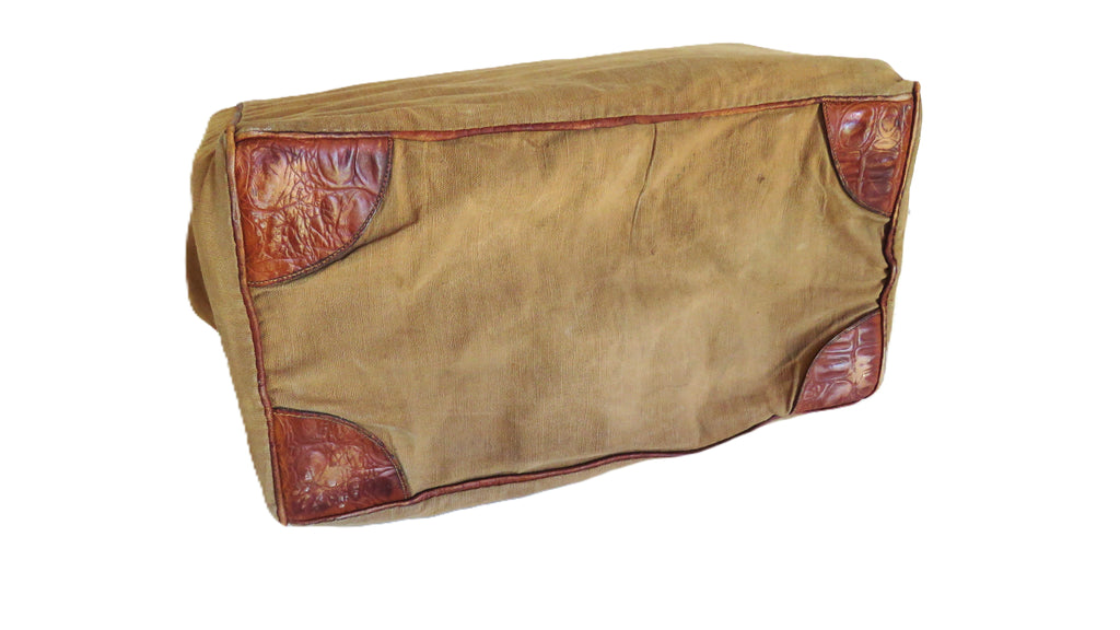 A vintage tan canvas bag with reddish-brown leather corner protectors, shown on a plain white background.
