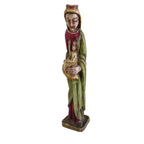 A small carved religious figurine of the Virgin Maryrobed holding a child, standing on a plain white surface against a white wall.