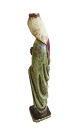 A small decorative figurine of a robed figure shown from the back, with a cream-colored head, green drapery, and a dark base, photographed against a plain light background.