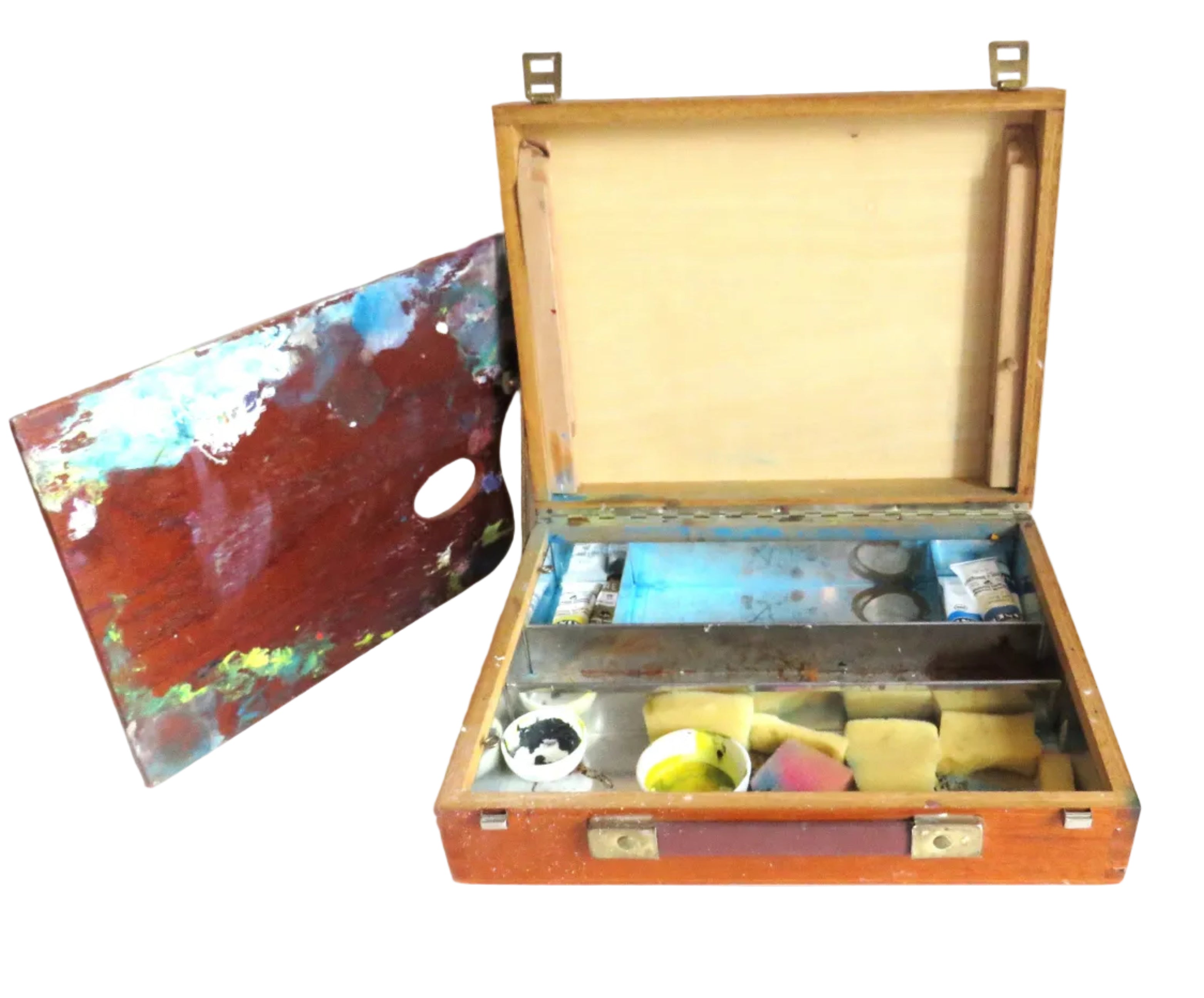 An open wooden artist's palette case with brass hardware, showing paint wells, brushes, and a palette with multicolored paint, set against a plain white background.
