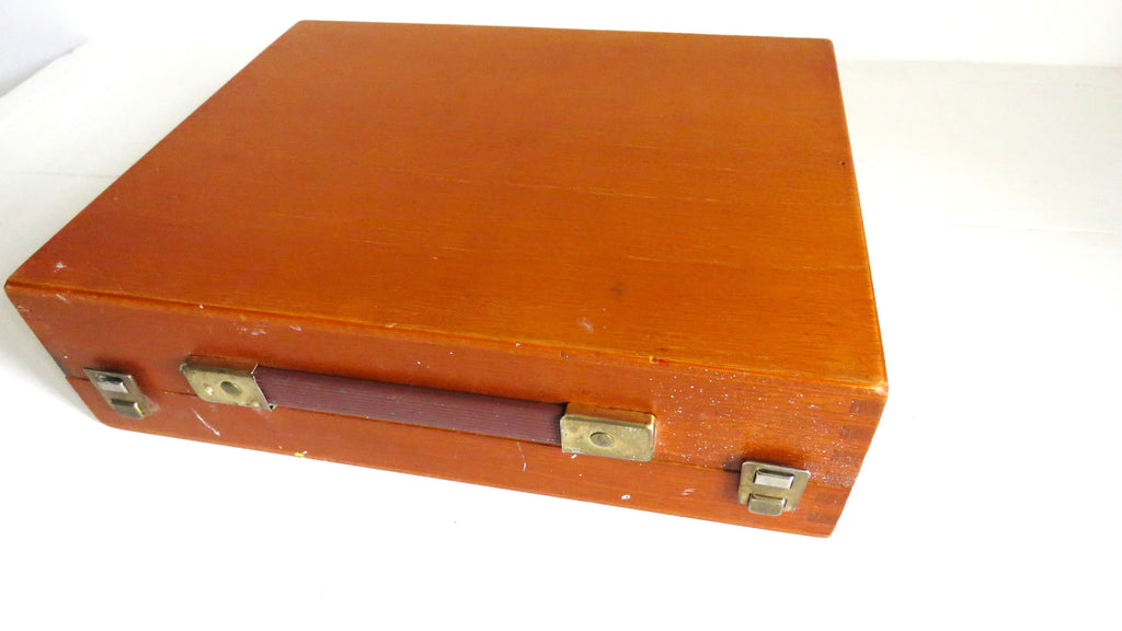 A vintage reddish-brown wooden art box with a leatherette handle and brass latches, shown on a plain white background.