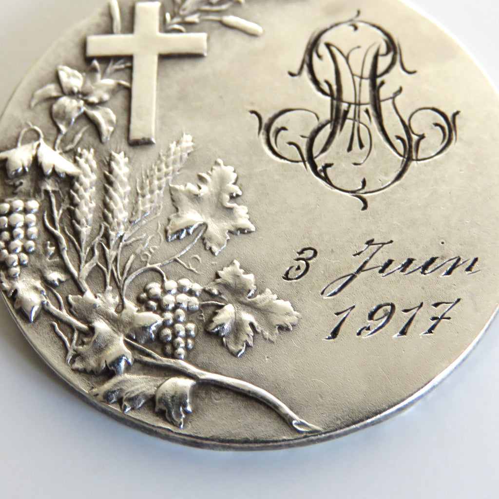A round silver commemorative coin or medallion with an embossed cross, grapevine leaves and grapes, a monogram, and the inscription '3 Juin 1917' on a plain light background.