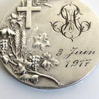 A round silver commemorative coin or medallion with an embossed cross, grapevine leaves and grapes, a monogram, and the inscription '3 Juin 1917' on a plain light background.