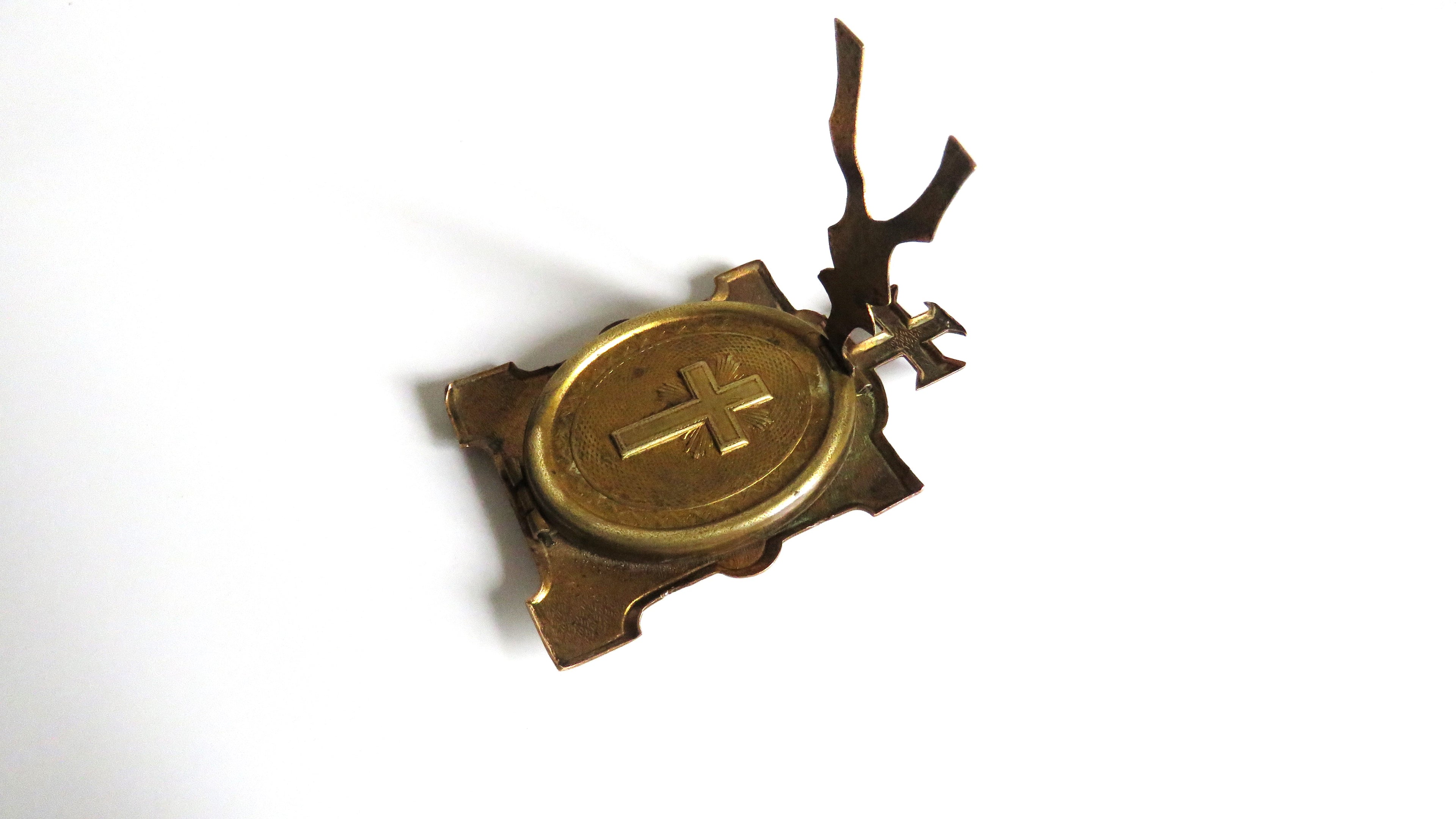 An antique brass religious pendant or medallion featuring a raised cross on an oval center, mounted on a rectangular bracket with a decorative upward-pointing finial, shown on a plain white background.
