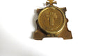A small antique brass religious pendant or medallion featuring a raised cross on a circular face, set against a plain white background.